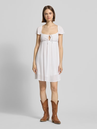 Frauenmodel trägt Babydoll Kleid aus Viskose mit Karree-Ausschnitt und Schleife von REVIEW, Gerader-Schnitt, Minikleid, Ganzkörperansicht von vorne.