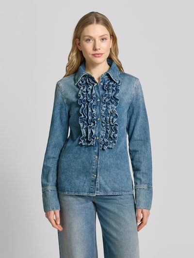Frauenmodel trägt Hemdbluse in Denim-Optik mit Rüschenbesatz Modell 'Dulce' von Mango aus reiner Baumwolle, taillierte Passform, Ganzkörperansicht von vorne.