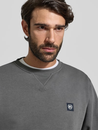 Męski model nosi Sweatshirt mit Rundhalsausschnitt und Label-Patch od Lerros, mieszanka bawełny, krój relaxed fit, naszywka z logo, szara tonacja, długość tyłu 72 cm, długość rękawów 66 cm, zdjęcie: zbliżenie na górną część ciała.