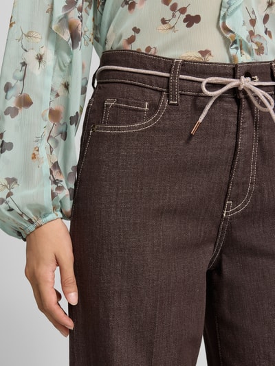 Frauenmodel trägt Wide Fit Jeans mit Viskose-Anteil von Marc Cain in Dunkelbraun, sichtbare Nähte, 5-Pocket-Design, Nahaufnahme Oberkörper, elastischer Baumwoll-Mix mit Viskose-Anteil und Bügelfalten, Detail aus Damen Jeans Kollektion.