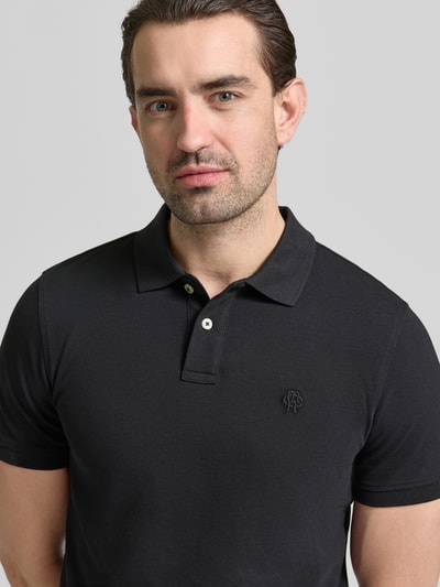 Männermodel trägt Slim Fit Poloshirt mit Logo-Stitching von MCNEAL in Schwarz, reine Baumwolle, Polokragen, Nahaufnahme Oberkörper.