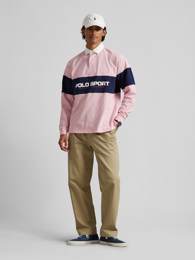 Männermodel trägt Regular Fit Poloshirt aus reiner Baumwolle von Polo Ralph Lauren in Rosa, Blau und Weiß, einfarbig, Langarm, Label-Schriftzug, Piqué-Textur, Ganzkörperansicht von vorne.
