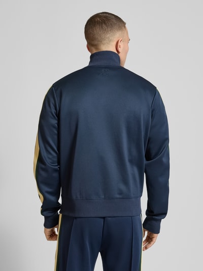 Männermodel trägt granatowa Track Jacket mit Stretch-Anteil Modell 'Everyday' von ANOTHER COTTON LAB, lampasy boczne, elastyczna mieszanka materiałów, prosta krój, wysoka stójka, zamek błyskawiczny, kieszenie zapinane na zamek, elastyczne wykończenia, aplikacja z metką, długość tyłu 63 cm w rozmiarze M, długość rękawów 68 cm w rozmiarze M, widok całej sylwetki z tyłu.