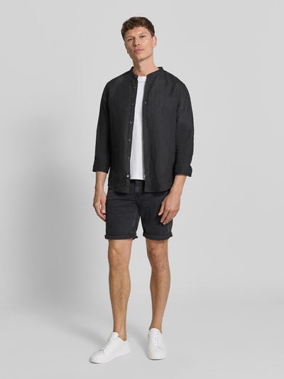 Männermodel trägt Slim Fit Jeansshorts aus Baumwoll-Mix Modell 'NAAILO' von Armedangels in Denim-Optik mit Label-Patch, 5-Pocket-Design, Beinabschluss mit Umschlag, Knopf und verdecktem Reißverschluss; Ganzkörperansicht von vorne.