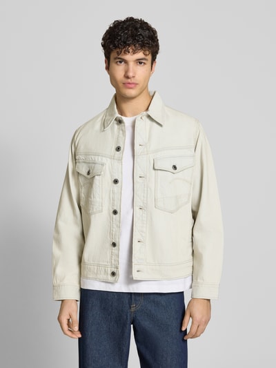 Męski model nosi Jeansjacke mit Brusttaschen Modell 'Dakota' von G-Star Raw, bawełniana, krój relaxed fit, beżowy kolor, widok całej sylwetki z przodu.