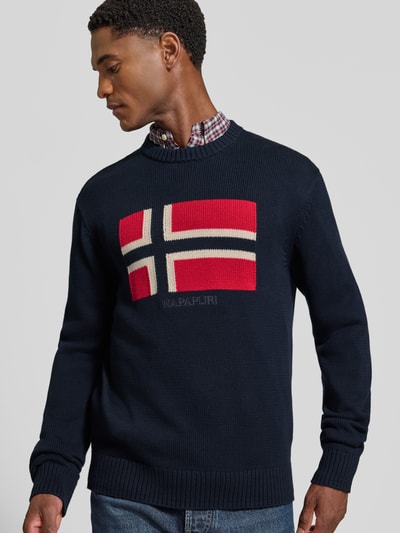 Mannenmodel draagt gebreide pullover uit puur katoen Model 'MURA' van Napapijri, recht pasvorm, ronde hals, ribboorden, marineblauw met rode en witte vlakken, ruglengte maat M 67 cm, mouwlengte maat M 70 cm, voorkant, close-up bovenlichaam.