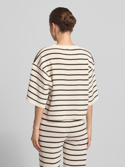 Frauenmodel trägt Oversized T-Shirt aus Viskose-Mix Modell 'NURIA' von VILLA SOPHIE mit Optik:Allover-Muster, Passform: Oversized, Label-Applikation, Rundhals-Ausschnitt, Ärmelform: Kurzarm, Materialverarbeitung: Rippstrick, in Weiß mit braunen Streifen, Ganzkörperansicht Rückansicht.
