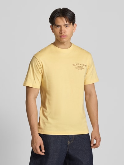 Männermodel trägt Regular Fit T-Shirt aus reiner Baumwolle Modell 'FRED' von Only & Sons in Optik: Unifarben mit Motiv-Print, Rundhals-Ausschnitt, Ärmelform: Kurzarm, Materialverarbeitung: Jersey, Ganzkörperansicht von vorne.