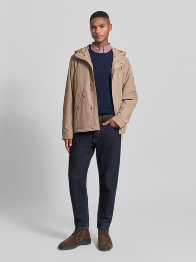 Mannelijk model draagt Regular Fit Funktionsjacke mit Kapuze van Tommy Hilfiger in beige, effen, waterafstotend, langem mouw, label patch, vooraanzicht hele lichaam.