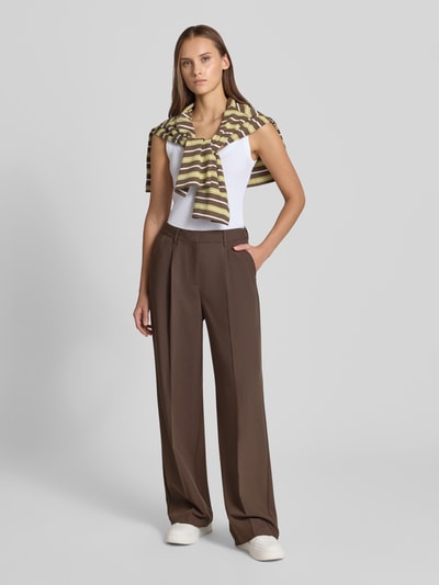 Frauenmodel trägt Wide Fit Hose mit Viskose-Anteil Modell 'Aya Ellis' von JJXX in Braun mit Bund- und Bügelfalten, Ganzkörperansicht von vorne.