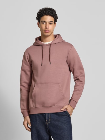 Męski model nosi Regular Fit Hoodie aus Baumwoll-Mix Modell 'CERES' od Only & Sons, gładki, dzianina sweat, różowy, z kieszenią kangurką i ściągaczami, marka widoczna, całkowity widok z przodu.