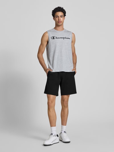 Männermodel trägt Shorts mit elastischem Bund und Label-Stitching von CHAMPION, schwarze Baumwoll-Mix-Shorts, Ganzkörperansicht von vorne.