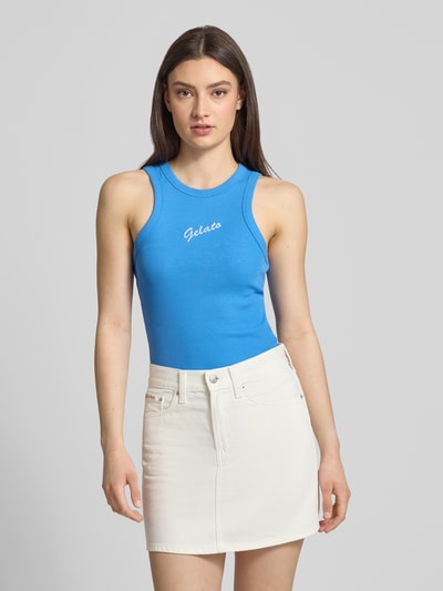 Frauenmodel trägt Trägertop in Ripp-Optik Modell 'FOREST' von JJXX in Blau mit weißem Schriftzug, kombiniert mit weißem Rock, Slim Fit, Baumwoll-Elasthan-Mix, Ganzkörperansicht von vorne.