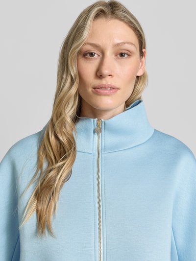 Frauenmodel trägt Blazer aus Viskose-Mix mit Stehkragen von Rinascimento in Hellblau, Reißverschluss mit Label-Detail, Nahaufnahme Oberkörper.