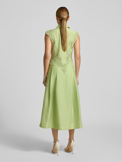 Frauenmodel trägt Hemdblusenkleid aus Modal-Mix mit Spitze Modell 'COLE' von Copenhagen Muse, A-Linie, Midikleid, Rückenlänge 128 cm, Brustweite 41 cm, sanftes Pastellgrün, geschwungene Spitzendetails, glatte Textur, Ganzkörperansicht Rückansicht.