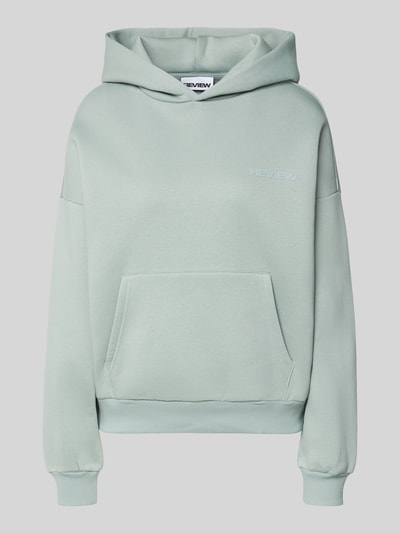 Frauenmodel trägt Hoodie mit Logo und Känguru-Tasche von Review, Baumwoll-Mix, Relaxed-Fit, pastellgrün, Ganzkörperansicht von vorne.