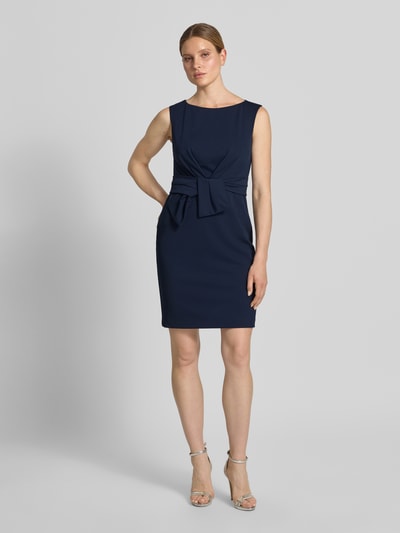 Frauenmodel trägt knielanges Cocktailkleid mit Knotendetail von Vera Mont, dunkelblau, gerader Schnitt, Material-Mix mit Stretch, Ganzkörperansicht von vorne.
