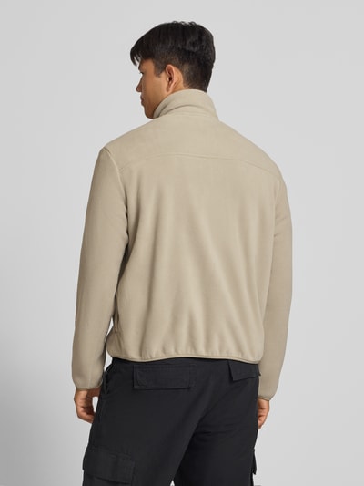 Männermodel trägt Fleecejacke mit Zweiwege-Reißverschluss Modell 'MASON' von JACK & JONES, beige, weiche Textur, Ganzkörperansicht Rückansicht, Herren Fleecejacke Regular Fit, Logo, Stehkragen, Eingrifftaschen, Rückenlänge und Ärmellänge bei Größe M jeweils 66 cm.