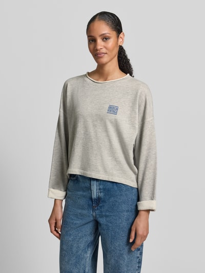 Frauenmodel trägt Oversized Sweatshirt mit Label-Print von American Vintage, beige Baumwoll-Mix, gerippter Rundhalsausschnitt, Nahaufnahme Oberkörper.