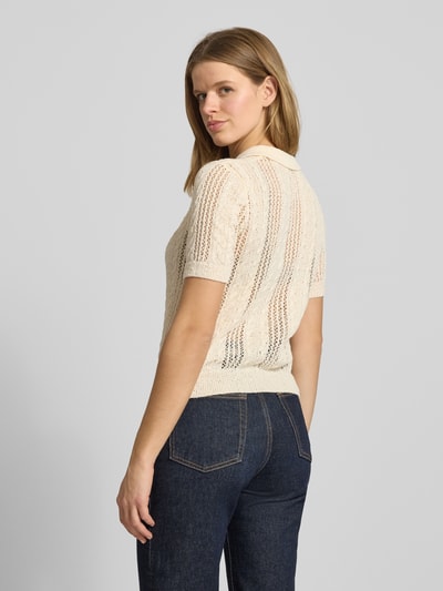 Frauenmodel trägt Slim Fit Poloshirt in Strick-Optik Modell 'Ajour' von Review in Creme mit Loch-Optik, Ganzkörperansicht Rückansicht.