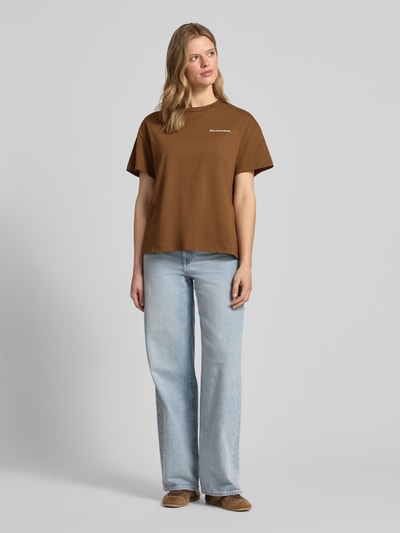 Frauenmodel trägt Relaxed Fit T-Shirt aus reiner Baumwolle - Special Drop von Marc O'Polo Denim, Optik: Unifarben, Passform: Relaxed-Fit, Applikation: Rückenprint, Label-Print, Rundhals, Ärmelform: Kurzarm, Material: Reine Baumwolle, Farbe: Braun, Hosen: Hellblau, Schuhe: Braun, Textur: Glatt, Ganzkörperansicht von vorne