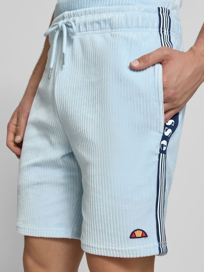 Mężczyzna nosi Shorts aus Cord Modell 'TOMATRO' od Ellesse, bawełniany miks ze stretchem, krój regular fit, jasnoniebieski, elastyczny pas, tunel, detailaufnahme bioder z przodu, szerokość w rozmiarze M: 42 cm, długość nogawki wewnętrznej w rozmiarze M: 21 cm.