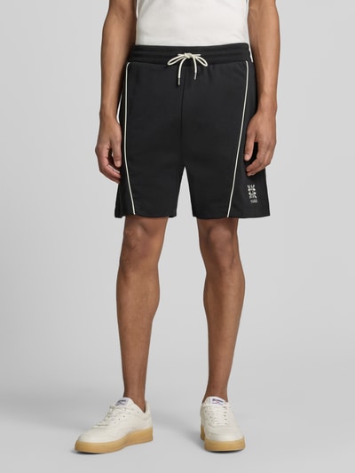 Männermodel trägt Regular Fit Sweatshorts aus Baumwoll-Mix Modell 'DARYNTO' von HUGO in Optik: Unifarben mit Kontraststreifen, Logo-Stitching, elastischem Bundabschluss mit Tunnelzug und seitlichen Eingrifftaschen vorne, Materialverarbeitung: Sweat, Vorderansicht, Nahaufnahme Unterkörper.