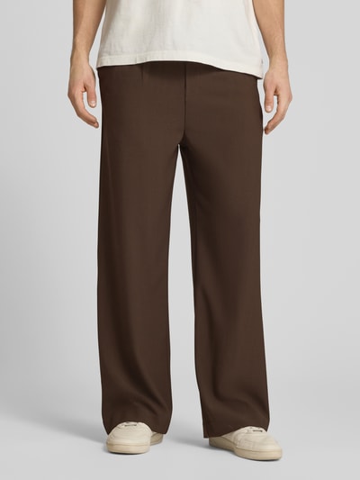 Männermodel trägt Stoffhose mit Logo-Bund und Gesäßtaschen von ANOTHER COTTON LAB, braun, Material-Mix mit Stretch-Anteil, Wide-Fit, Ganzkörperansicht von vorne.