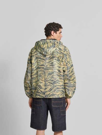 Männermodel trägt Regular Fit Windbreaker mit Kapuze von Kenzo mit Allover-Animal-Print, Reißverschluss, Busttaschen, Rückenlänge 69 cm, Schulterbreite 60 cm, Ärmellänge 64 cm, Farbmix aus Gelb, Schwarz und Beige, strukturierte Oberfläche, Ganzkörperansicht Rückansicht.