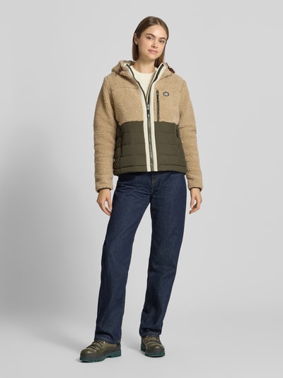 Kobieta modelka nosi Regular Fit Jacke mit Teddyfellbesatz od Superdry, beżowy i oliwkowy kolor, kaptur z tunelem, zamek błyskawiczny, kieszenie napoleonki i wpuszczane, długość tyłu w rozmiarze S: 58 cm, szerokość ramion w rozmiarze S: 42 cm, szerokość w rozmiarze S: 44 cm, długość rękawów w rozmiarze S: 63 cm, widok całej sylwetki z przodu.
