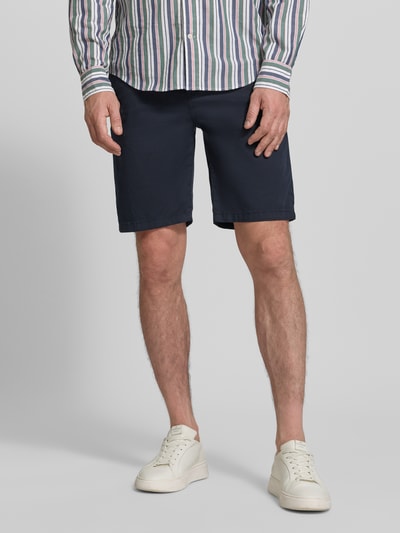 Männermodel trägt Tapered Chinoshorts aus Baumwoll-Mix von BOSS Orange in Dunkelblau, Optik: Unifarben, Materialverarbeitung: Twill, Ganzkörperansicht von vorne.