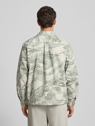 Männermodel trägt Regular Fit Hemdjacke mit Rumpftunnelzug Modell 'LELDON' von BOSS Orange mit Allover-Camouflage-Muster in hellen Grüntönen, langarm, Druckknöpfe, Label Stitching, Rückenpasse mit Cacharel-Falte, Manschetten, seitliche Eingrifftaschen mit Druckknöpfen, Ganzkörperansicht Rückansicht.