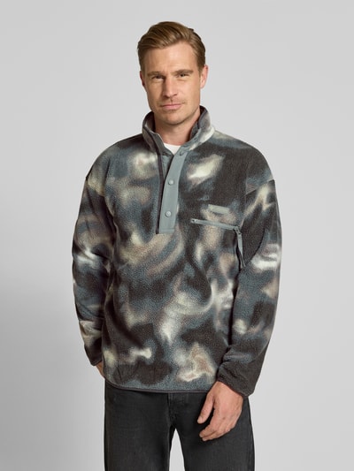 Männermodel trägt Fleecepullover mit Label-Patch Modell 'HELVETIA' von Columbia in Grau mit abstraktem Muster und Brusttasche, Ganzkörperansicht von vorne. Rückenlänge 73 cm, Ärmellänge 60 cm, Stehkragen, kurze Knopfleiste.