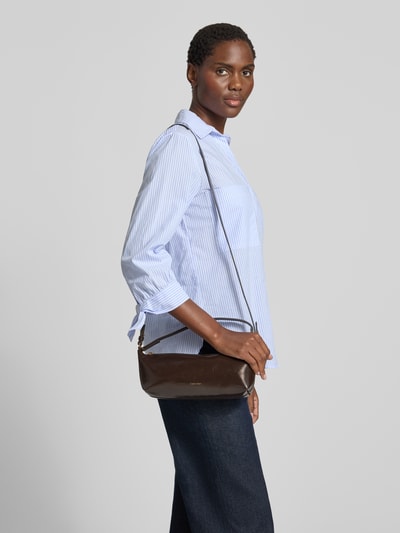 Kobieta nosi torebkę Henkeltasche mit Label-Prägung model 'FOIL LOGO GLOSSY CONV BAG' od CK Calvin Klein, brąz, skóra, z wytłaczanym logo. Ganzkörperansicht z przodu