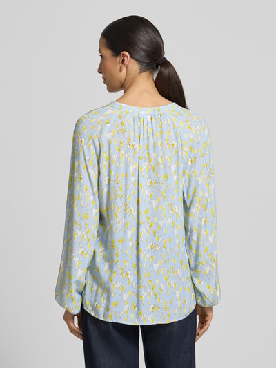 Frauenmodel trägt Regular Fit Bluse aus reiner Viskose mit Allover-Motiv-Print von Emily Van den Bergh in Blau mit gelbem Muster, Tunika-Ausschnitt, langärmeliges Design, elastische Ärmelabschlüsse, Rückenlänge 68 cm, Ärmellänge 65 cm, Ganzkörperansicht Rückansicht.