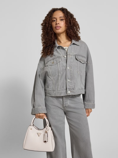 Frauenmodel trägt Handtasche mit Label-Applikation Modell 'ECO MERIDIAN II' von Guess, beige mit Tragehenkel und Schulterriemen, Hauptfach mit Reißverschluss, Maße 30x21x12 cm, Länge Schulterriemen 122 cm, Ganzkörperansicht von vorne.