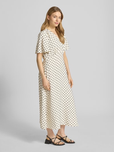 Modelka kobieca ma na sobie Midikleid mit V-Ausschnitt Modell 'ZABBY' od ICHI, kremowa sukienka w czarne grochy, fason A-linia, dekolt w serek, rękawy nietoperz, długość tyłu w rozmiarze 36: 124 cm, szerokość w rozmiarze 36: 44 cm, długość rękawa w rozmiarze 36: 26 cm, widok całej sylwetki z przodu.