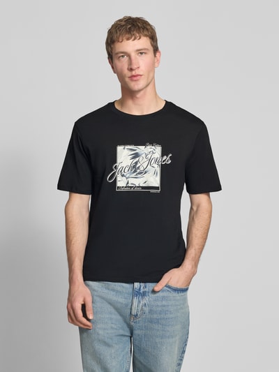 Männermodel trägt Herren T-Shirt mit Print aus Reine Baumwolle, Regular-Fit, Rundhalsausschnitt, Produktname: T-Shirt mit Rundhalsausschnitt Modell 'HONOLULU' von Jack & Jones, Rückenlänge bei Größe M 68 cm, dunkle Grundfarbe, Ganzkörperansicht von vorne.