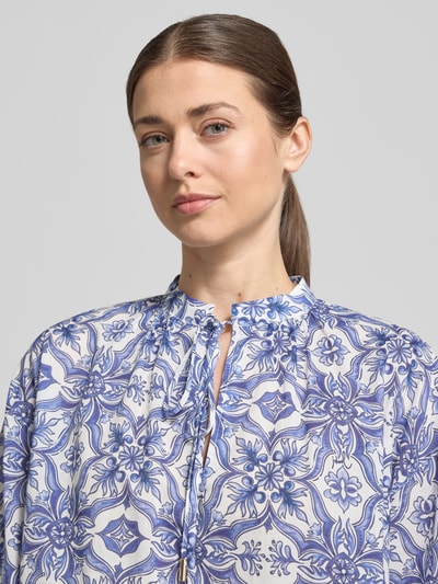Kobieta modelka nosi bluzkę Regular Fit Bluse mit Schlüsselloch-Ausschnitt Modell 'Beyda' od JOOP!, mieszanka modalu, wzór na całej powierzchni, wycięcie w kształcie łezki, wiązanie, rękaw o dł. 3/4, długość tyłu 58 cm, długość rękawów 32 cm, kolor biało-niebieski, faktura gładka, zbliżenie na górną część ciała.