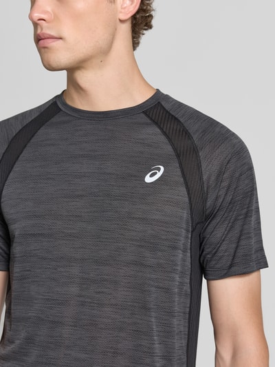 Męski model nosi Regular Fit T-Shirt mit Logo-Print Model 'Road' von ASICS TIGER, półprzezroczysty materiał, okrągły dekolt, Długość tyłu w rozmiarze M: 69 cm, kolor czarny, szara melanżowa faktura, widoczne panele siateczkowe, nadruk z logo, półzbliżenie górnej części ciała