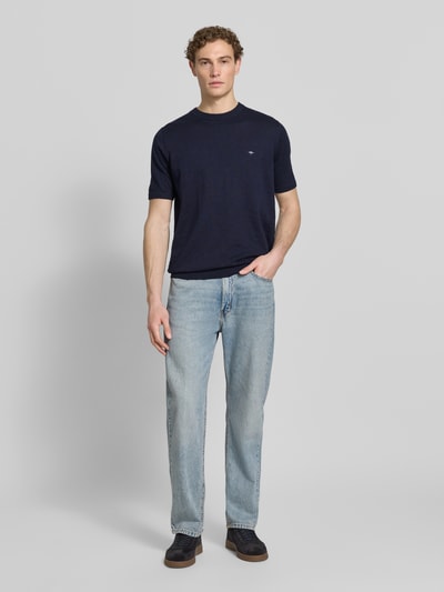 Męski model nosi Regular Fit T-Shirt mit Leinen-Anteil in Strick-Optik od Fynch-Hatton, imitacja dzianiny, mieszanka bawełny i lnu, krój regular fit, wyhaftowane logo, elastyczne wykończenia, długość tyłu w rozmiarze M: 70 cm, granatowy kolor, gładka faktura, widok całej sylwetki z przodu.