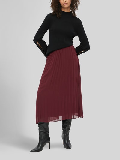 Frauenmodel trägt Plisseerock mit schwingendem Volantsaum von S. OLIVER BLACK LABEL in Weinrot, unifarben, Faltenoptik, Midi-Länge, Ganzkörperansicht von vorne.