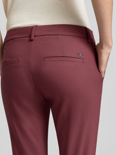 Vrouwenmodel draagt Slim Fit Anzughose aus Baumwoll-Mix von MOS MOSH in bordeaux, gladde structuur, mix van katoen en elastaan, gestileerde achterzakken, riemlussen, knoop- en ritssluiting, bandwijdte maat 36: 39 cm, binnenbeenlengte maat 36: 76 cm, detailopname rugaanzicht.