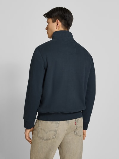 Męski model trägt Sweatshirt mit Reißverschluss und Label-Stitching von Superdry, mieszanka bawełny, krój regular fit, stójka, długość tyłu w rozmiarze M 67 cm, długość rękawów w rozmiarze M 69 cm, widok całej sylwetki od tyłu.