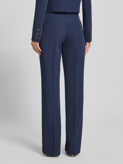 Frauenmodel trägt Hose mit Gürtel Modell 'LEILA' von Guess, dunkelblauer Material-Mix mit Stretch-Anteil, Flared-Cut, Ganzkörperansicht Rückansicht.