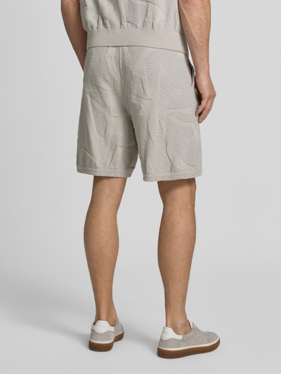 Männermodel trägt Regular Fit Sweatshorts aus Baumwoll-Mix Modell 'ASURFER' von BOSS Orange, Optik: Unifarben, Struktur, Label-Patch, Bundabschluss elastisch mit Tunnelzug, Eingrifftaschen, Materialverarbeitung: Frottee, Farbe beige, Ganzkörperansicht Rückansicht.