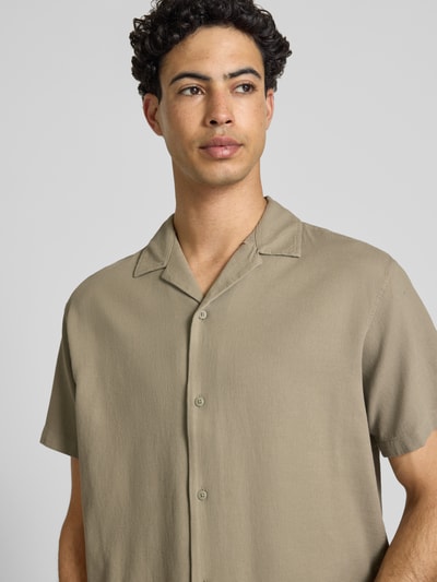 Męskimodel nosi Regular Fit koszulę casualową z fakturowanym wzorem model 'Global' od Jack & Jones z bawełny, z krótkim rękawem, kołnierzem z połami oraz listwą guzikową. Długość tyłu w rozmiarze M: 71 cm, szerokość ramion w rozmiarze M: 51 cm, długość rękawów w rozmiarze M: 25 cm. Kolory stonowane, gładka faktura. Nahaufnahme górnej części ciała.