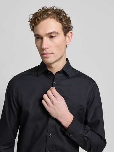 Männermodel trägt Regular Fit Freizeithemd mit Logo-Stitching Modell 'New' von OLYMP in Schwarz mit Kentkragen, Langärmelig, Brusttasche, durchgehende Knopfleiste, Sportmanschetten, reine Baumwolle; Nahaufnahme Oberkörper.