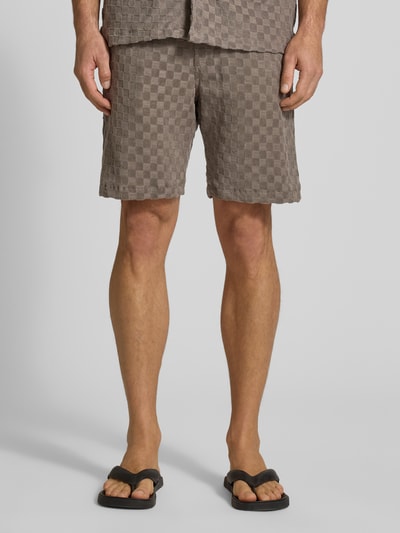 Mężczyznamodel nosi Regular Fit Shorts mit Label-Patch od Lindbergh, bawełniana mieszanka, kolor taupe, krój regular fit, kieszenie boczne i tylna, szerokość w rozmiarze M: 45 cm, długość wewnętrzna nogawki w rozmiarze M: 22 cm, tekstura w kratkę, widok całej sylwetki z przodu.