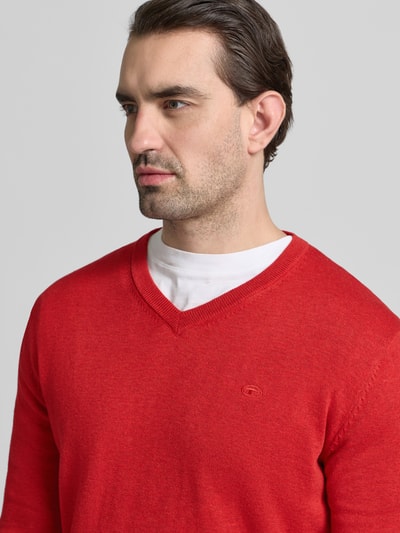 Männermodel trägt Regular Fit Pullover aus reiner Baumwolle von Tom Tailor in uni rot, feinstrick, V-hals, logo-stitching, langarm, nahaufnahme oberkörper.